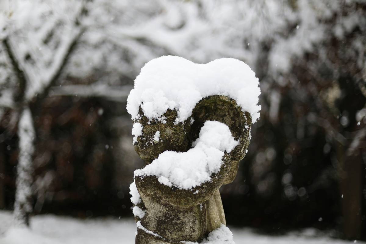 Cast stone angel statue softly lit with warm-white LED uplights in a snow-dusted garden with evergreen garlands